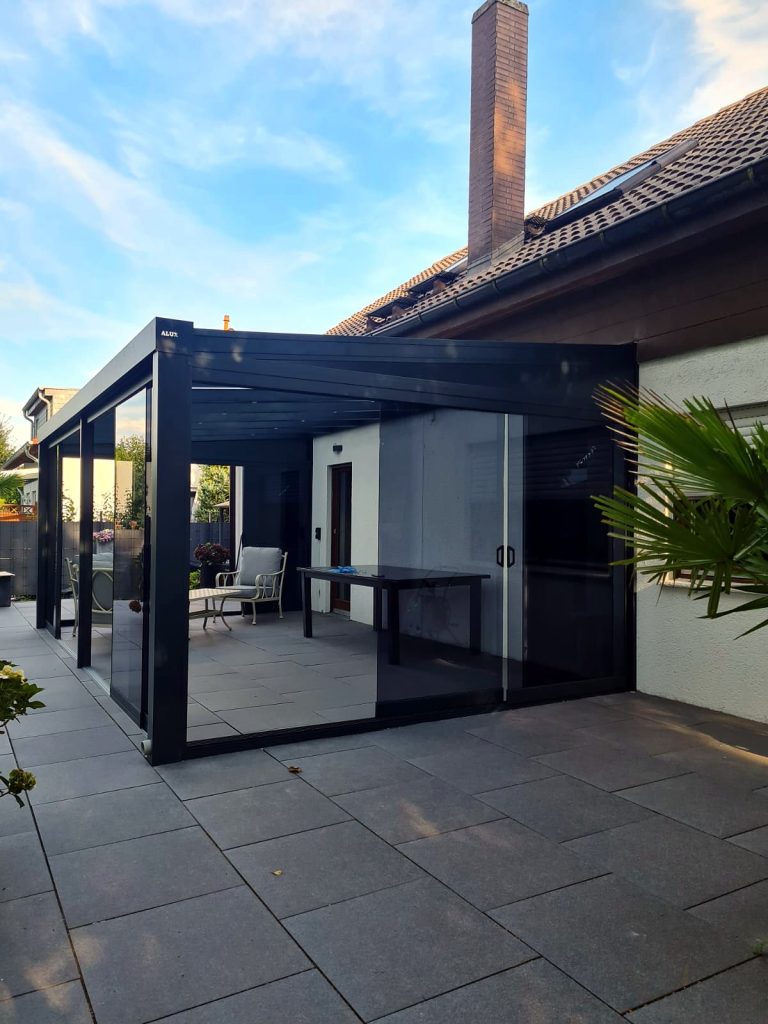 Anthrazitfarbener Glas-Terrassenraum mit Glasschiebewänden an einem Wohnhaus