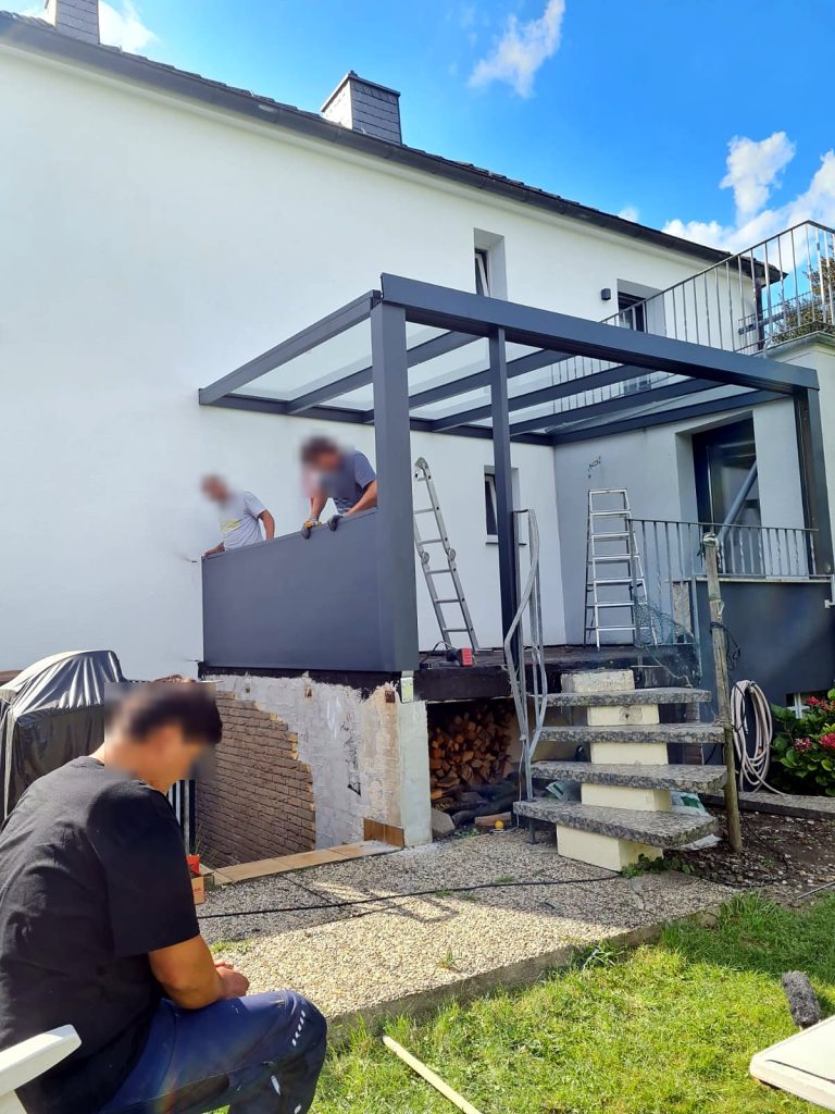 Monteure bauen eine Glasdach-Überdachung über einer erhöhten Terrasse mit Treppe