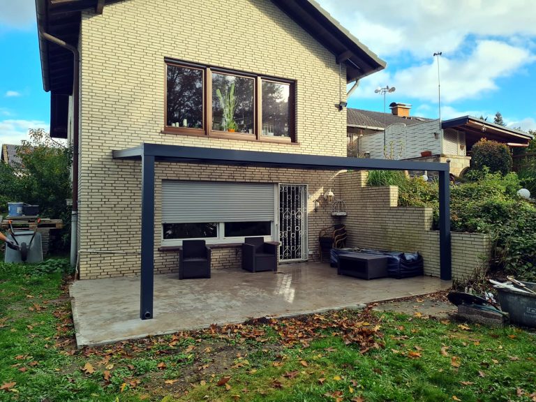 Fertige anthrazitfarbene Terrassenüberdachung im Garten eines Klinkerhauses
