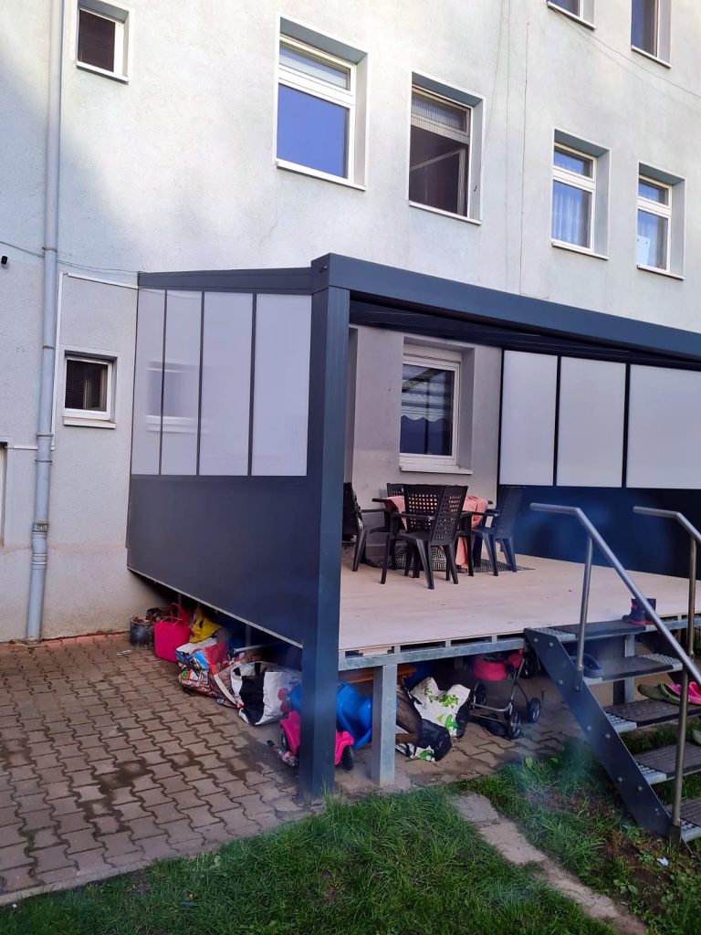 Überdachte erhöhte Terrasse mit seitlicher Wand aus Milchglas-Elementen